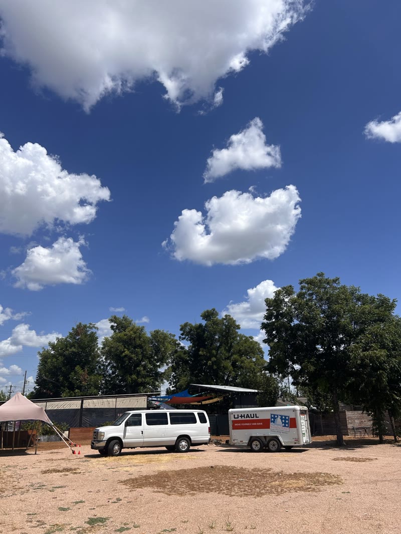 A white tour van and trailer parked under a wide blue sky